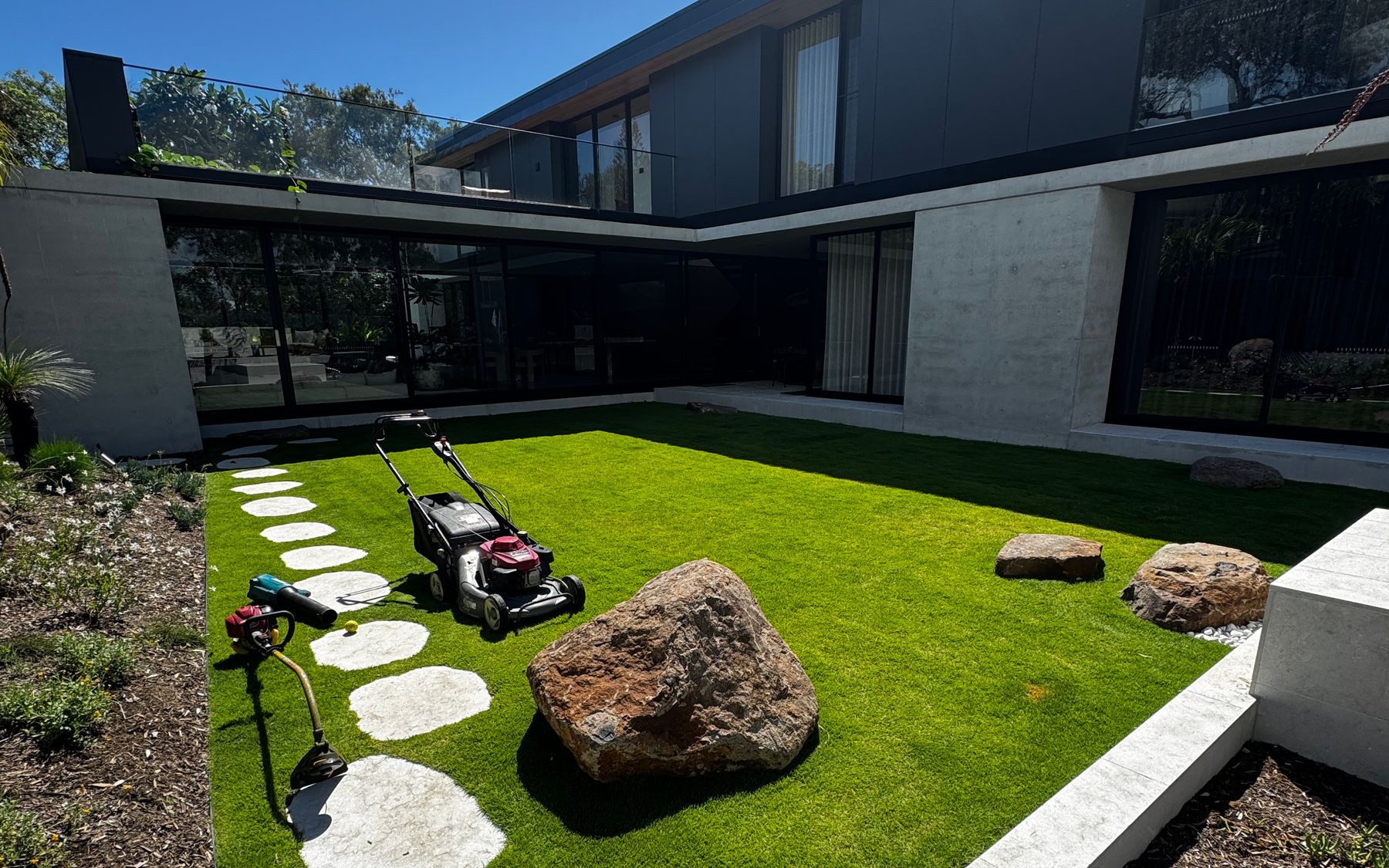 Neat green lawn with round stepping stones and a large boulder in the courtyard of a modern house