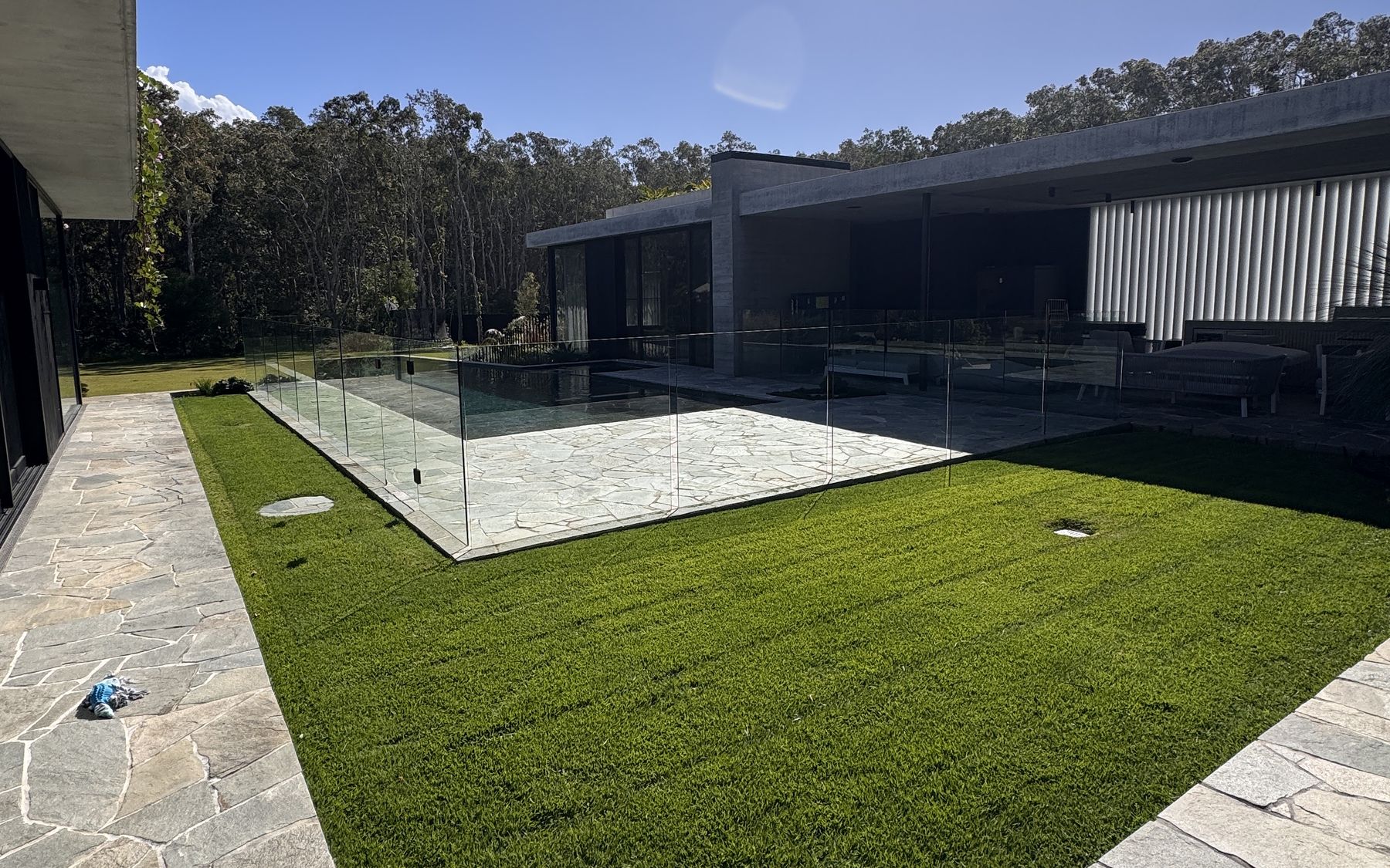 Freshly mown, striped green lawn framed by stone paving next to a glass-fenced pool